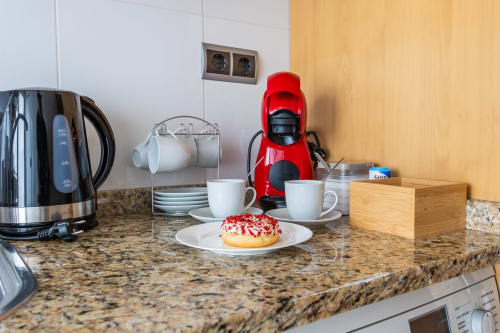 Kitchen counter with red coffee maker, kettle, cups, pastry, and wooden organizer at Haus Holiday Homes apartment