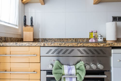 Modern kitchen with stainless steel oven, granite countertop, wooden knife block, and green checkered oven mitts at Haus