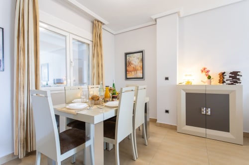 Modern dining area in Haus Holiday Homes apartment with white furniture, gold curtains, and pool view in San Pedro del