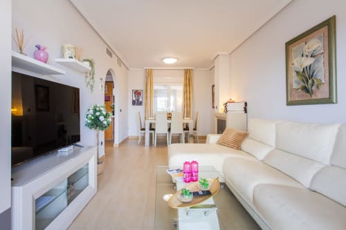 Modern open-plan apartment living area with cream sofa, TV, dining table, and kitchen at Haus Holiday Homes in San Pedro del