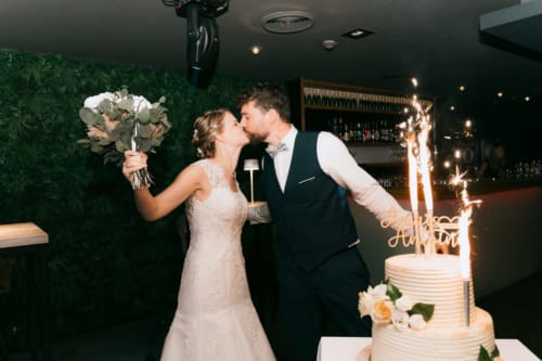 Bride and groom kissing at Ô Château hotel in Hayange, France, with wedding cake and sparklers
