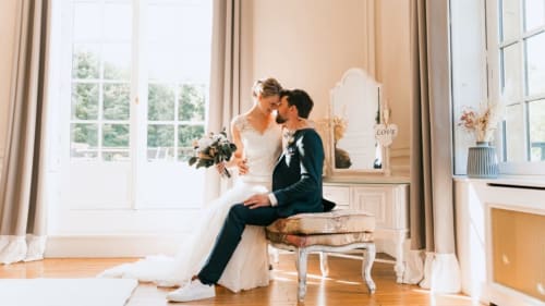 Newlyweds embrace by window at Ô Château hotel in Hayange, elegant bridal suite with natural light