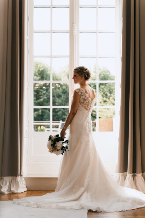 Bride in white lace wedding dress at Ô Château hotel in Hayange, France, holding black and white bouquet