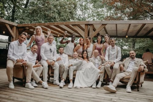 Large group of guests in neutral tones posing on wooden deck under pergola at Ô Château hotel in Hayange, France