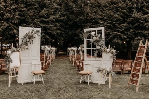 Outdoor wedding ceremony setup at Ô Château in Hayange with white doors, decorated chairs, and greenery lining the aisle