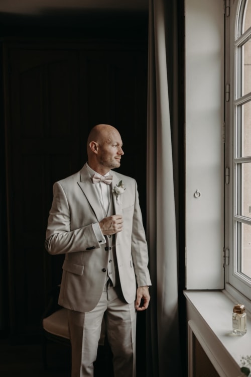 Groom in beige suit at Ô Château hotel window in Hayange, France