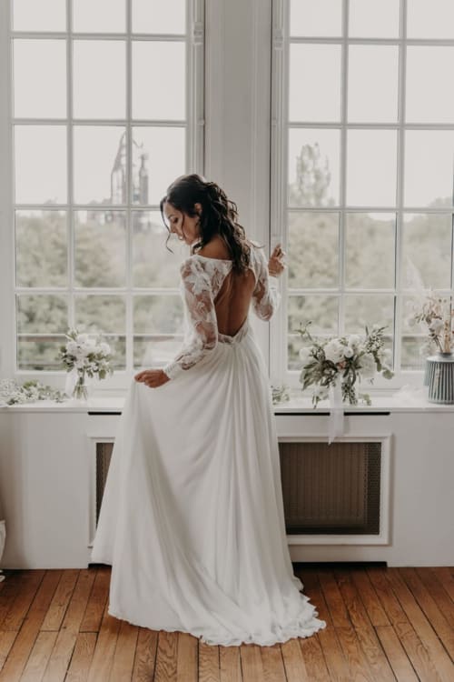 Bride in elegant white lace gown at Ô Château hotel, Hayange, overlooking scenic landscape