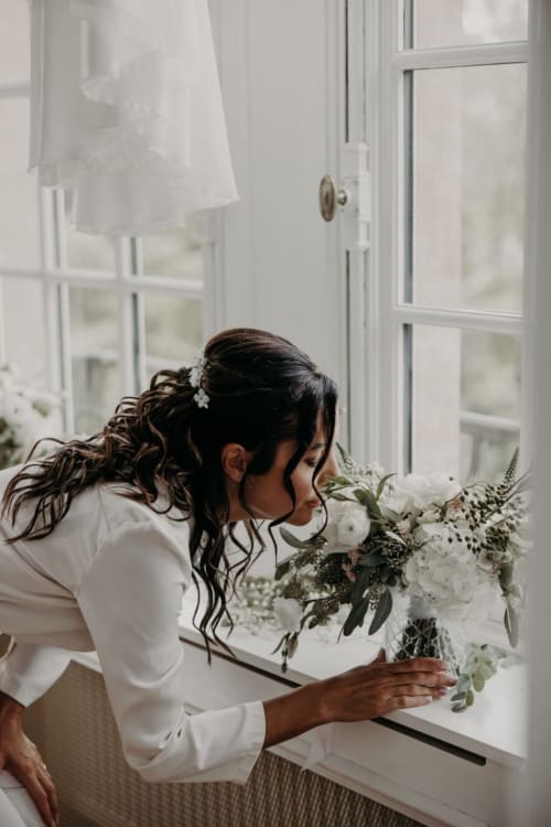 Bride in white dress with white floral bouquet at Ô Château hotel window in Hayange