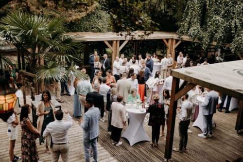 Guests mingling at Ô Château's outdoor garden reception under wooden pergolas with ivy-covered walls in Hayange