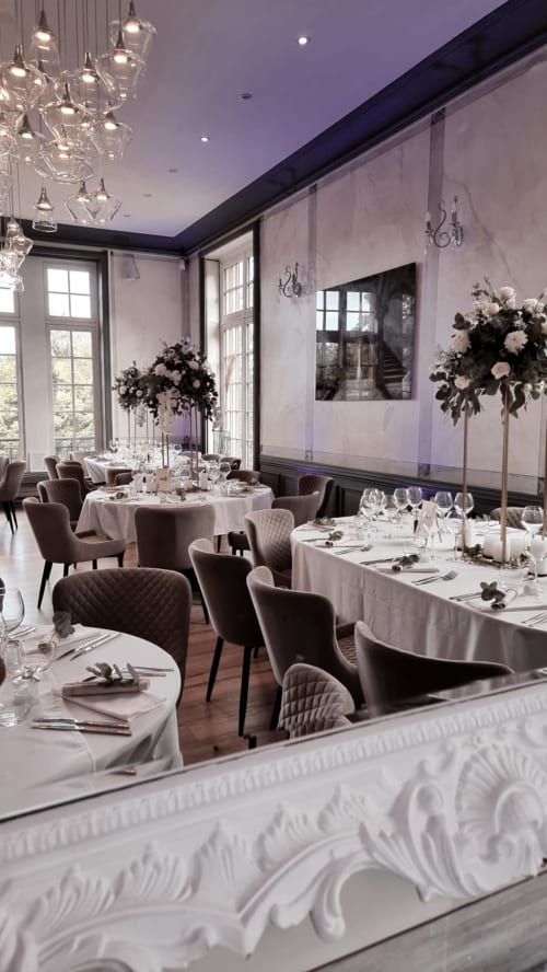 Elegant fine dining room at Ô Château in Hayange with round and rectangular tables, chandeliers, and purple ambient lighting