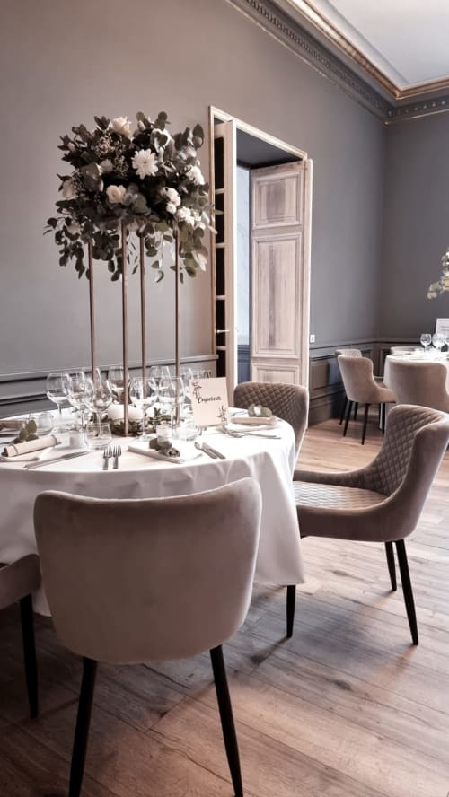 Elegant dining room at Ô Château Hayange with round table, tall floral centerpiece, upholstered chairs
