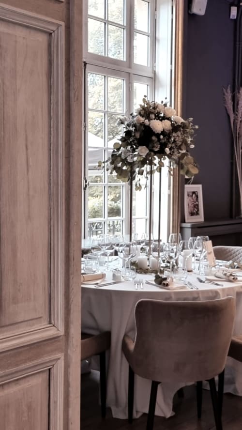 Elegant dining room at Ô Château Hayange with tall windows, round table, floral centerpiece, and classic French décor
