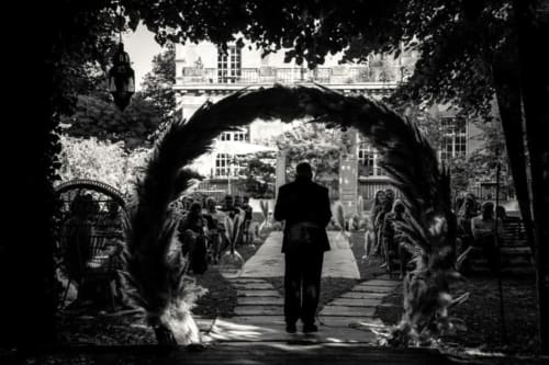 Man in suit walking through ivy-covered garden archway toward Ô Château hotel in Hayange, black and white
