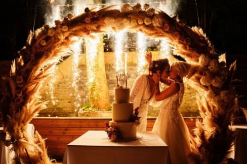 Bride and groom cutting wedding cake under ornate golden arch at Ô Château hotel in Hayange