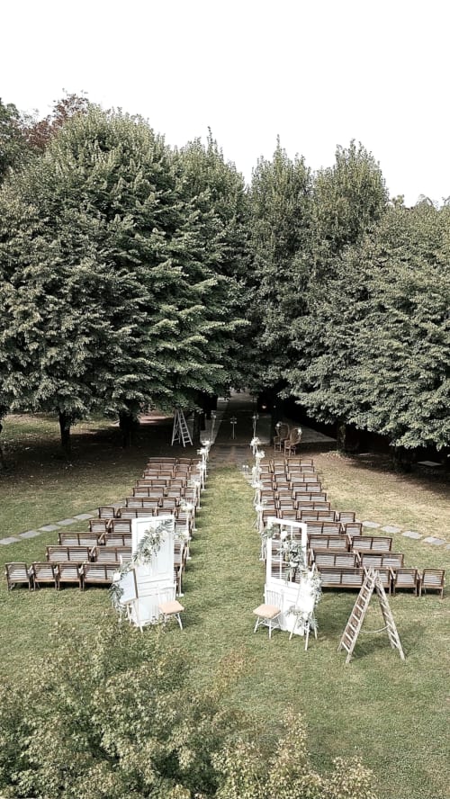 Outdoor wedding ceremony setup at Ô Château in Hayange with wooden chairs and decorated aisle surrounded by tall trees