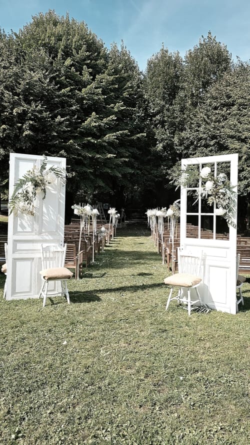 Elegant outdoor wedding ceremony setup at Ô Château in Hayange with white doors, flower arrangements, and tree-lined garden