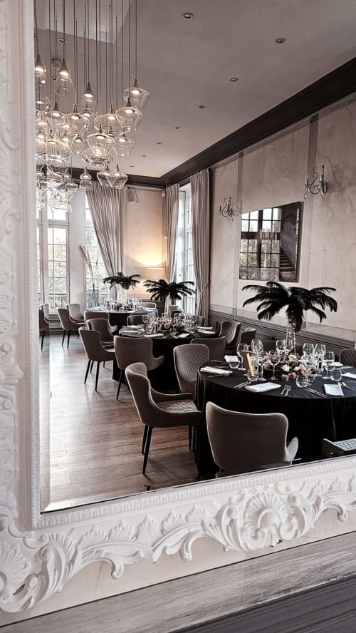 Elegant dining room at Ô Château hotel in Hayange with crystal pendant lights, black tables, and tall windows overlooking