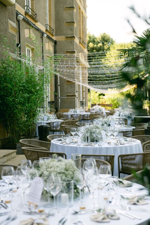 Elegant outdoor dining setup at Ô Château Hayange with white tablecloths, greenery, and modern string lighting