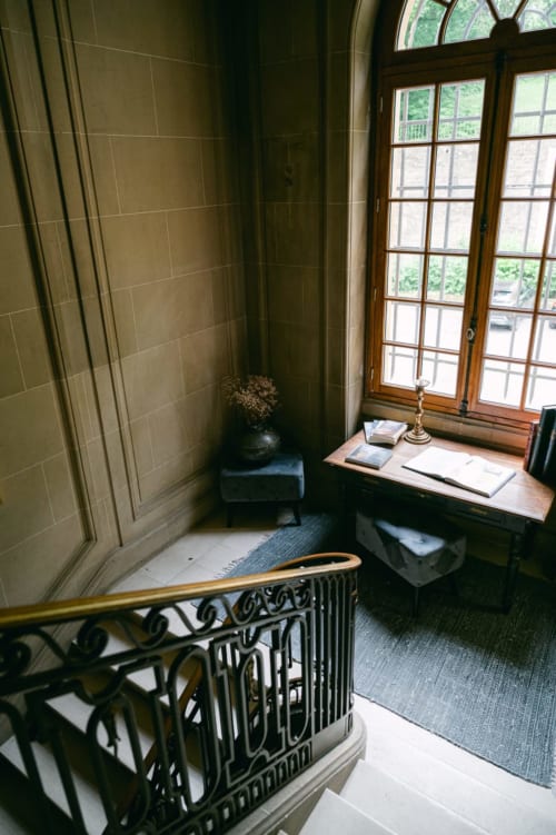 Elegant Ô Château hotel landing featuring ornate staircase railing, wooden desk by tall windows overlooking Hayange gardens