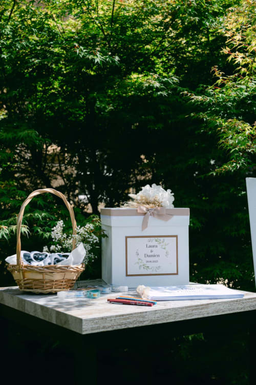 Wedding guest book and wicker basket displayed on table at Ô Château hotel in Hayange with lush green garden backdrop