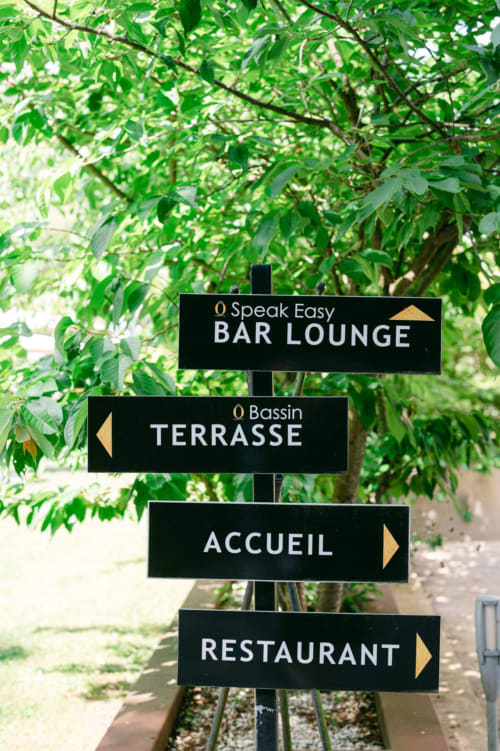 Directional signs for Ô Château hotel in Hayange showing Bar Lounge, Terrasse, Accueil, and Restaurant with green foliage