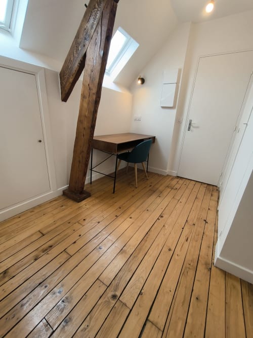Espace de travail cosy à la Conciergerie La Parisienne avec bureau en bois, chaise, poutres apparentes et puits de lumière