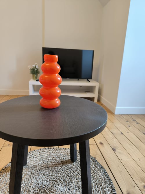 Élégant salon moderne avec table ronde noire, vase décoratif rouge, télévision et parquet à la Conciergerie La Parisienne