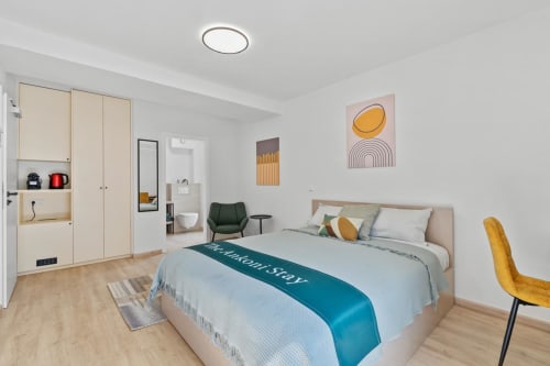 Modern bedroom at Mattbnb Metz featuring queen bed, yellow chair, kitchenette, and geometric wall art