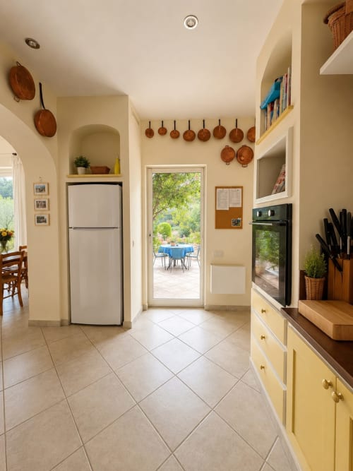 Cuisine lumineuse à la Conciergerie Maurin à Arles avec murs crème, batterie de cuivre, vue sur patio et équipements modernes