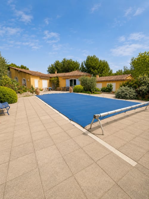 Bâche bleue sur piscine rectangulaire de la villa Conciergerie Maurin à Arles, France, avec bâtiment jaune et verdure