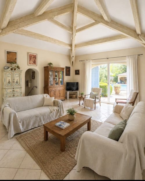 Séjour lumineux avec poutres apparentes, mobilier crème, table basse en bois et vue sur la piscine à Conciergerie Maurin
