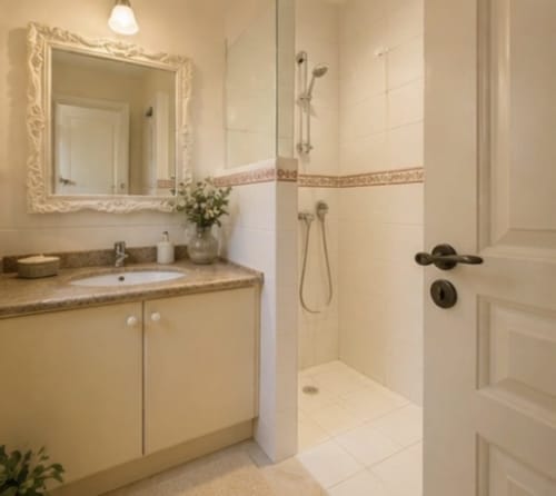 Salle de bains élégante à la Conciergerie Maurin à Arles avec carrelage crème, douche ouverte, vasque et miroir raffiné
