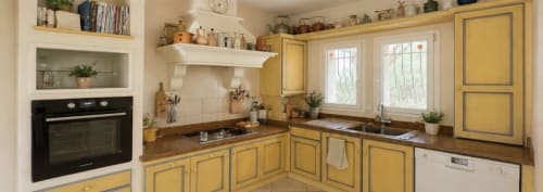 Cuisine jaune avec plan de travail en bois, four intégré, cuisinière et coin repas à la Conciergerie Maurin à Arles