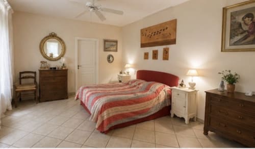 Chambre spacieuse à la Conciergerie Maurin à Arles avec lit capitonné rouge, literie rayée, mobilier bois et décoration crème