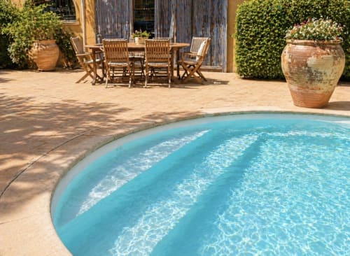 Piscine turquoise cristalline, patio en terre cuite, mobilier en bois et murs de lierre à la Conciergerie Maurin à Arles