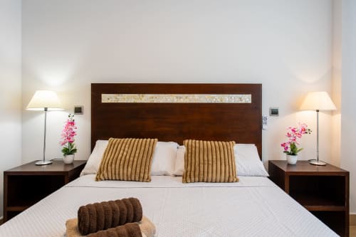 Modern bedroom at Haus Holiday Homes with dark wood headboard, white bedding, gold pillows, and bedside lamps with pink