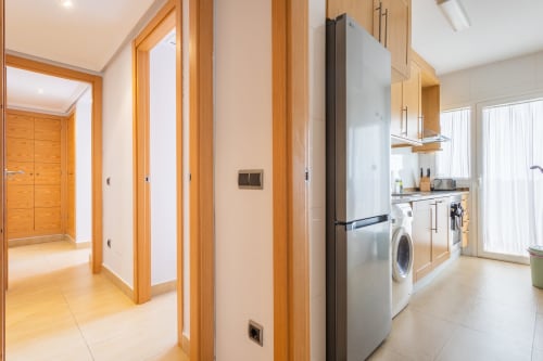 Modern kitchen with stainless steel appliances, wooden cabinetry, and open living space in Apto. Plus Ultra apartment at Haus