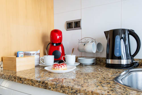 Kitchen counter with red coffee maker, black kettle, white cups, and pastry at Haus Holiday Homes, San Pedro del Pinatar