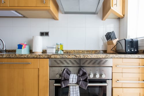 Modern kitchen with wooden cabinets, granite countertop, stainless steel oven, and knife block at Haus Holiday Homes