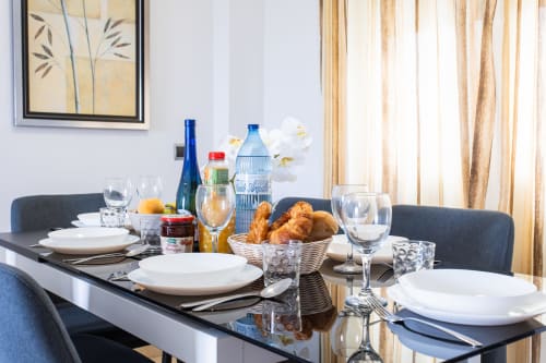 Elegant dining table set with white plates, wine glasses, bread basket, and blue bottles at Haus Holiday Homes apartment in