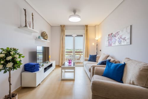 Modern apartment living room with beige sofa, blue pillows, TV, white shelving, and balcony access at Haus Holiday Homes, San