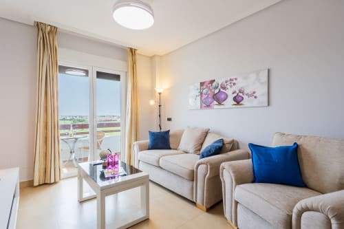 Bright living room in San Pedro del Pinatar apartment with beige sofa, blue pillows, balcony view, and floral wall art