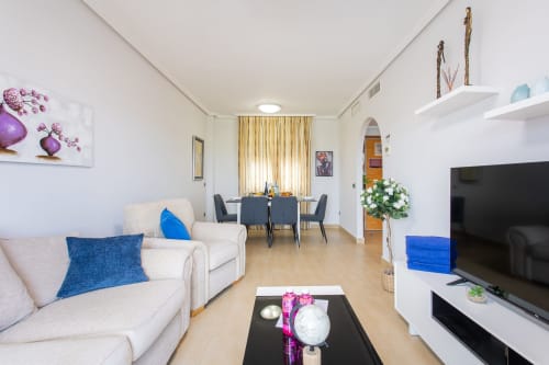 Modern living room in Haus Holiday Homes apartment with cream sofas, blue accents, dining area, and flat-screen TV in San