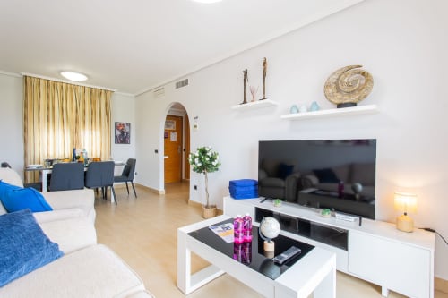 Modern living room with TV, white furniture, and dining area in Apto. Plus Ultra apartment at Haus Holiday Homes, San Pedro