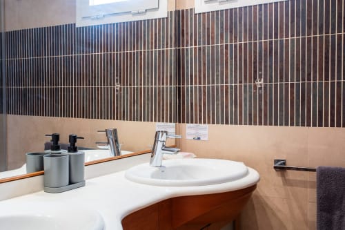 Modern bathroom with curved white sink, wood vanity, and brown tile accent wall in San Pedro del Pinatar apartment