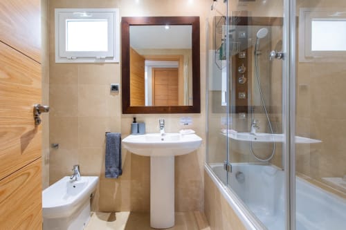 Modern bathroom with pedestal sink, dark-framed mirror, glass shower enclosure, and wood-grain accents in Apto. Plus Ultra at