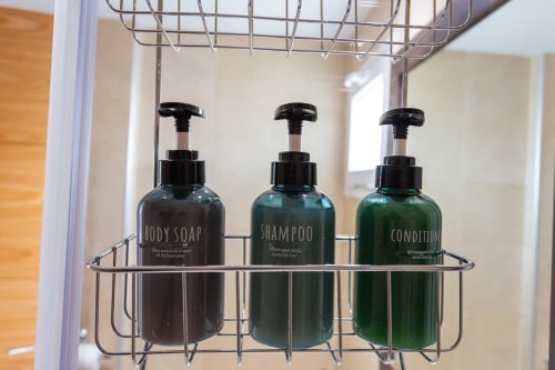 Three pump bottles of body soap, shampoo, and conditioner in a wire shower caddy at Haus Holiday Homes apartment