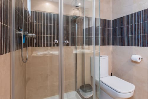 Modern bathroom at Haus Holiday Homes with glass shower enclosure, striped tile accents, toilet, and beige tiling in San