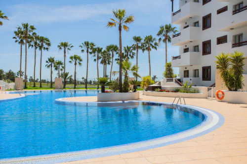 Curved swimming pool with palm trees and white apartment building at Haus Holiday Homes, San Pedro del Pinatar