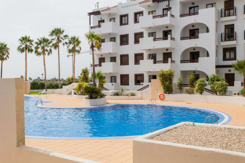 Blue swimming pool with curved edges at Haus Holiday Homes in San Pedro del Pinatar, white apartment building with palm trees